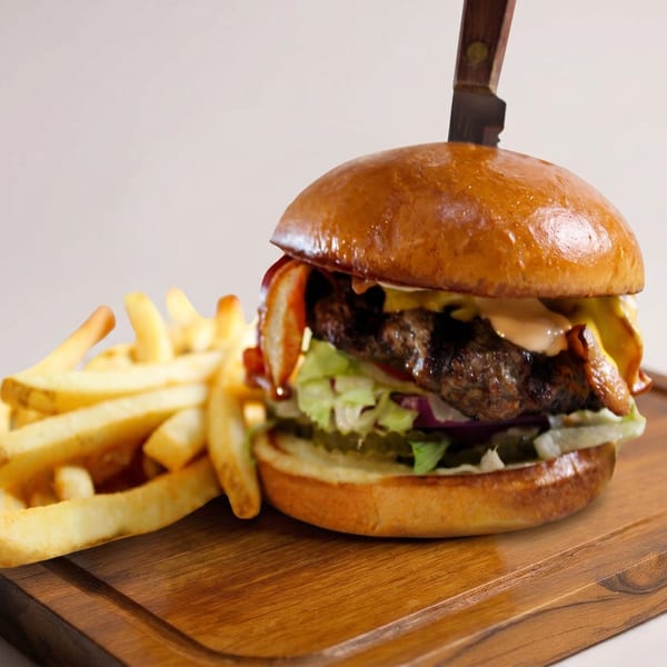 Gourmet burger with bacon, cheese, lettuce, and sauce, skewered with a knife, served with fries.